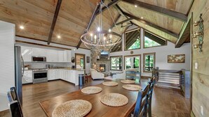 A spacious kitchen with a large island, a dining area with a wooden table and woven placemats, and a stone fireplace. - Outdoor Barrel Sauna, Hot Tub, Fire Pit, 2 Full Kitchens, (Morganton)