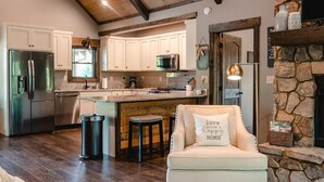 A modern kitchen with white cabinets, a stainless steel refrigerator, and a stone fireplace. - Outdoor Barrel Sauna, Hot Tub, Fire Pit, 2 Full Kitchens, (Morganton)