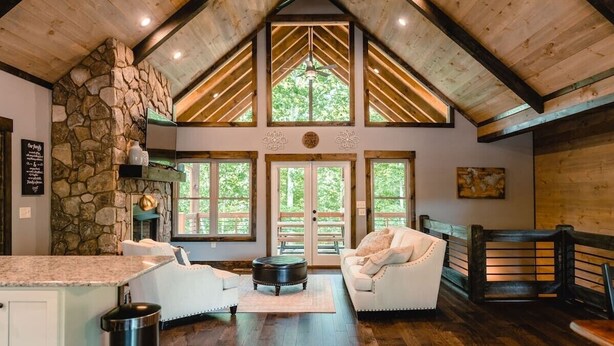 A spacious living area with a stone fireplace, a large window, and a cozy seating arrangement. - Outdoor Barrel Sauna, Hot Tub, Fire Pit, 2 Full Kitchens, (Morganton)