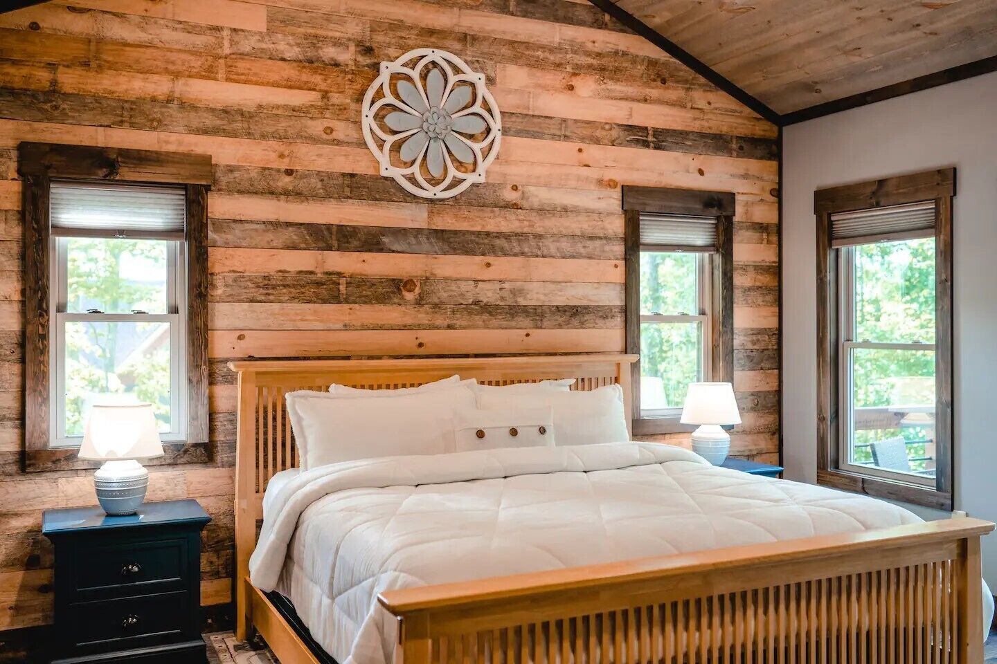 A wooden cabin bedroom with a bed, two windows, and a decorative wall piece.