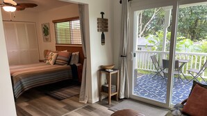 A cozy bedroom with a bed, a small table, and a view of a balcony. - Kaloli Point retreat 3 blocks from the ocean and minutes to Shipman Beach trail! (Keaau)