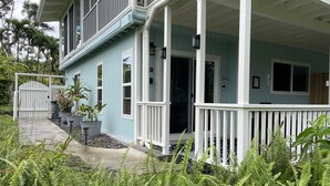 A two-story house with a porch, a gated entrance, and surrounding greenery. - Kaloli Point retreat 3 blocks from the ocean and minutes to Shipman Beach trail! (Keaau)