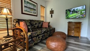 A living room with a patterned sofa, a television, a wooden cabinet, and a lamp. - Kaloli Point retreat 3 blocks from the ocean and minutes to Shipman Beach trail! (Keaau)