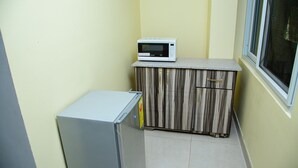 A compact kitchen with a microwave on a countertop, a small refrigerator, and a cabinet with a striped pattern. - Ark Hotel and Apartments (Accra)