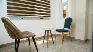 A room with a brown upholstered chair, a blue upholstered chair with a gold frame, and a small round table. - Ark Hotel and Apartments (Accra)