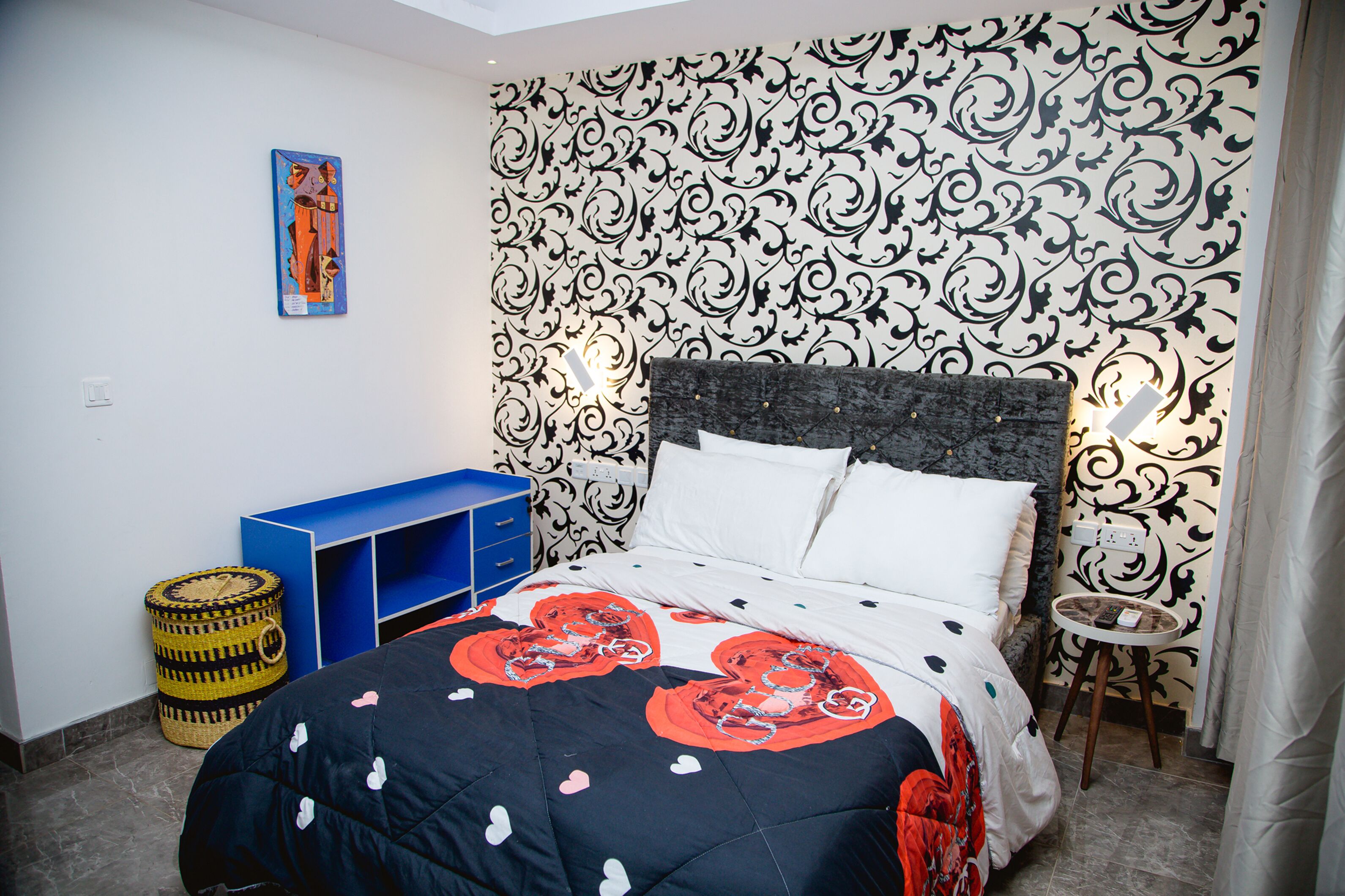 Une chambre avec un lit, un meuble de rangement bleu, un mur décoratif et une petite table.