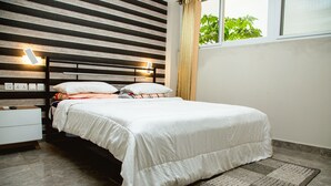 A neatly made bed with white bedding, a bedside table with a lamp, and a window with curtains. - Ark Hotel and Apartments (Accra)