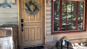 Una puerta de madera con un adorno floral, una ventana con vista a árboles y un escalón de piedra que lleva a la puerta.