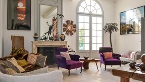 A spacious living room with a fireplace, two purple armchairs, a white sofa, and a large arched window providing natural light. - Beautiful home in Léognan with sauna (Léognan)