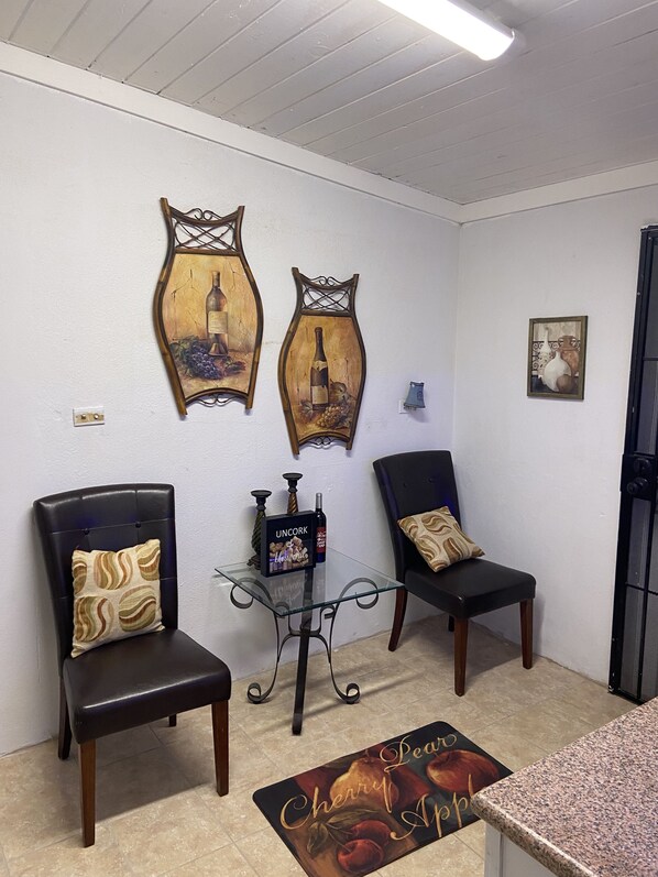 A room with two leather chairs, a small table with a wine bottle, and wall art depicting wine bottles and grapes.
