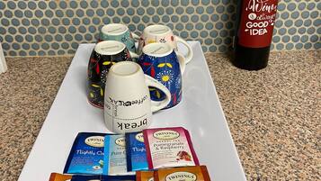 A tray with Twinings herbal tea bags, a bottle of wine, and decorative mugs on a granite countertop.