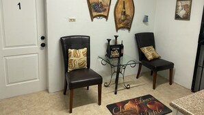 A hallway with two black leather chairs, a glass table with a bottle and a sign, and artwork on the walls. - Rosebud (Rock Sound)