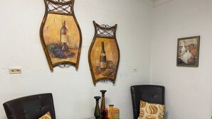 A room with two black leather chairs, a glass table with a bottle and candle, and two wall-mounted paintings. - Rosebud (Rock Sound)