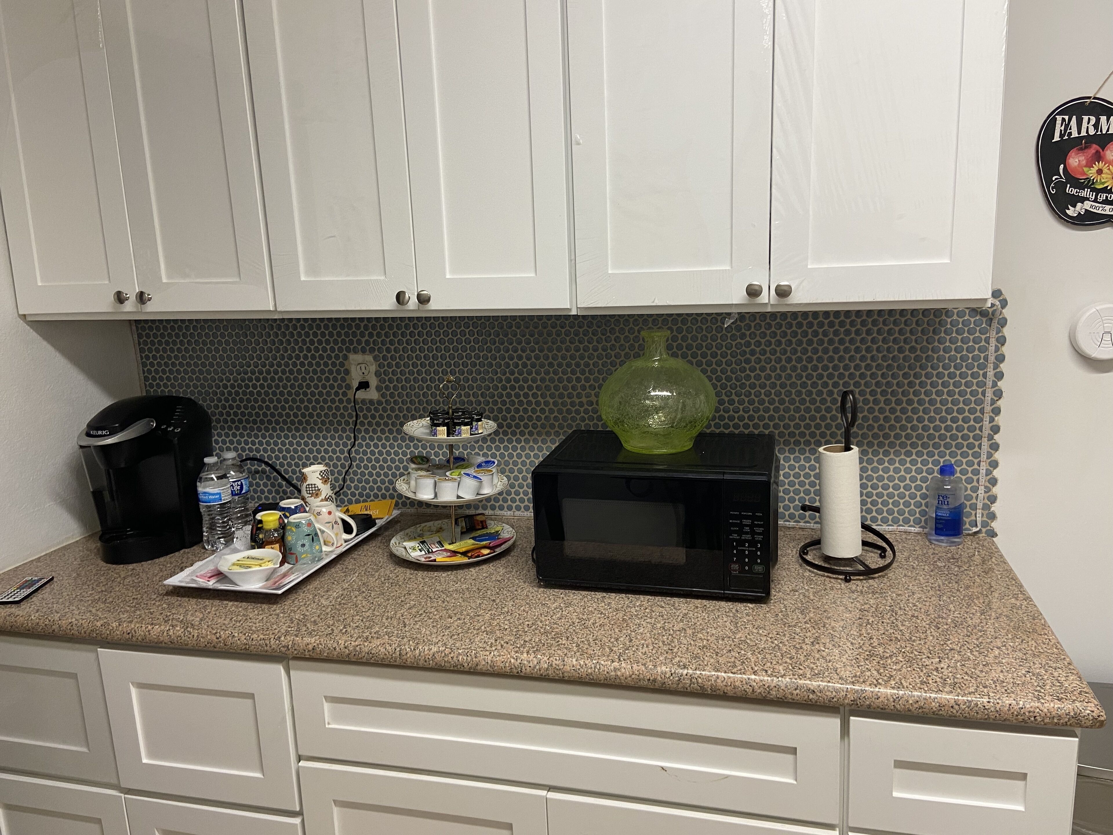 Una cocina con gabinetes blancos, microondas, cafetera y dispensador de agua.