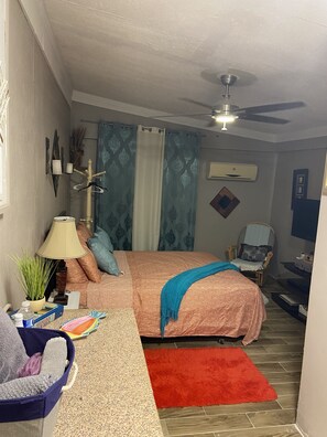 A bedroom with a bed, a chair, a desk, a red rug, and a ceiling fan.
