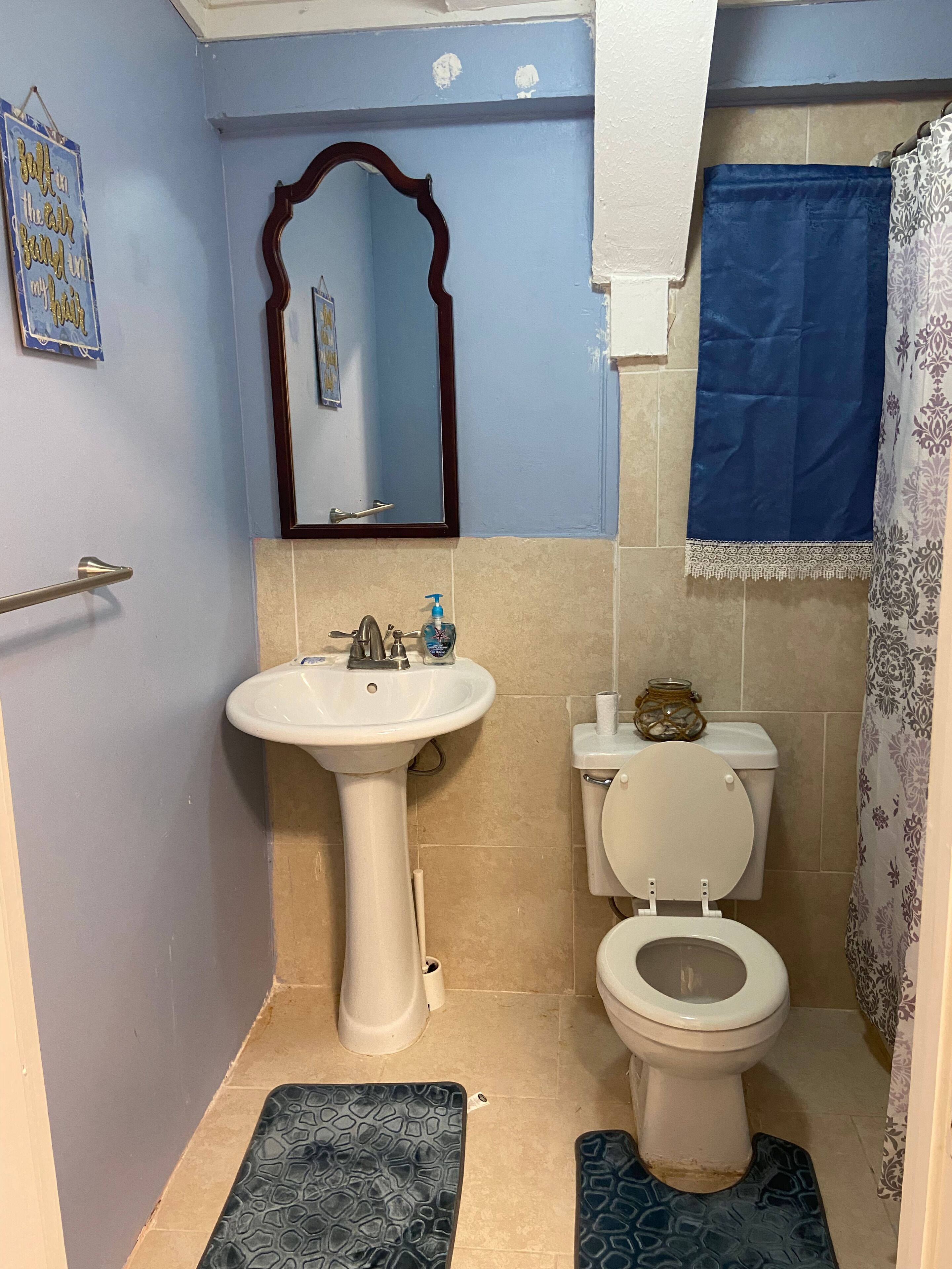 A bathroom with a pedestal sink, toilet, and a mirror with a decorative frame.