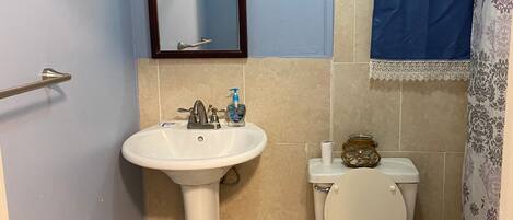 A bathroom with a pedestal sink, toilet, and a mirror with a decorative frame.