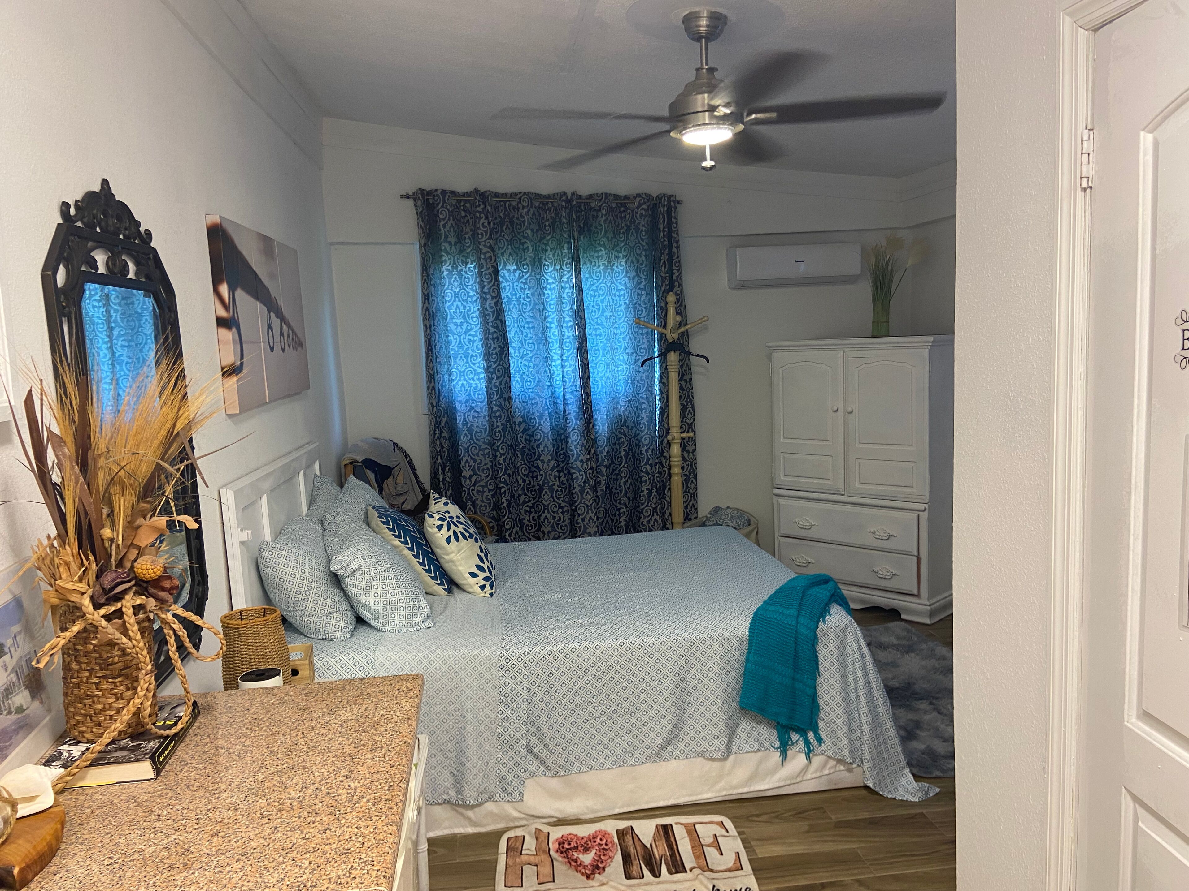 A bedroom with a bed, a ceiling fan, a dresser, and a decorative wall piece.