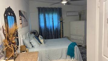 A bedroom with a bed, a ceiling fan, a dresser, and a decorative wall piece.