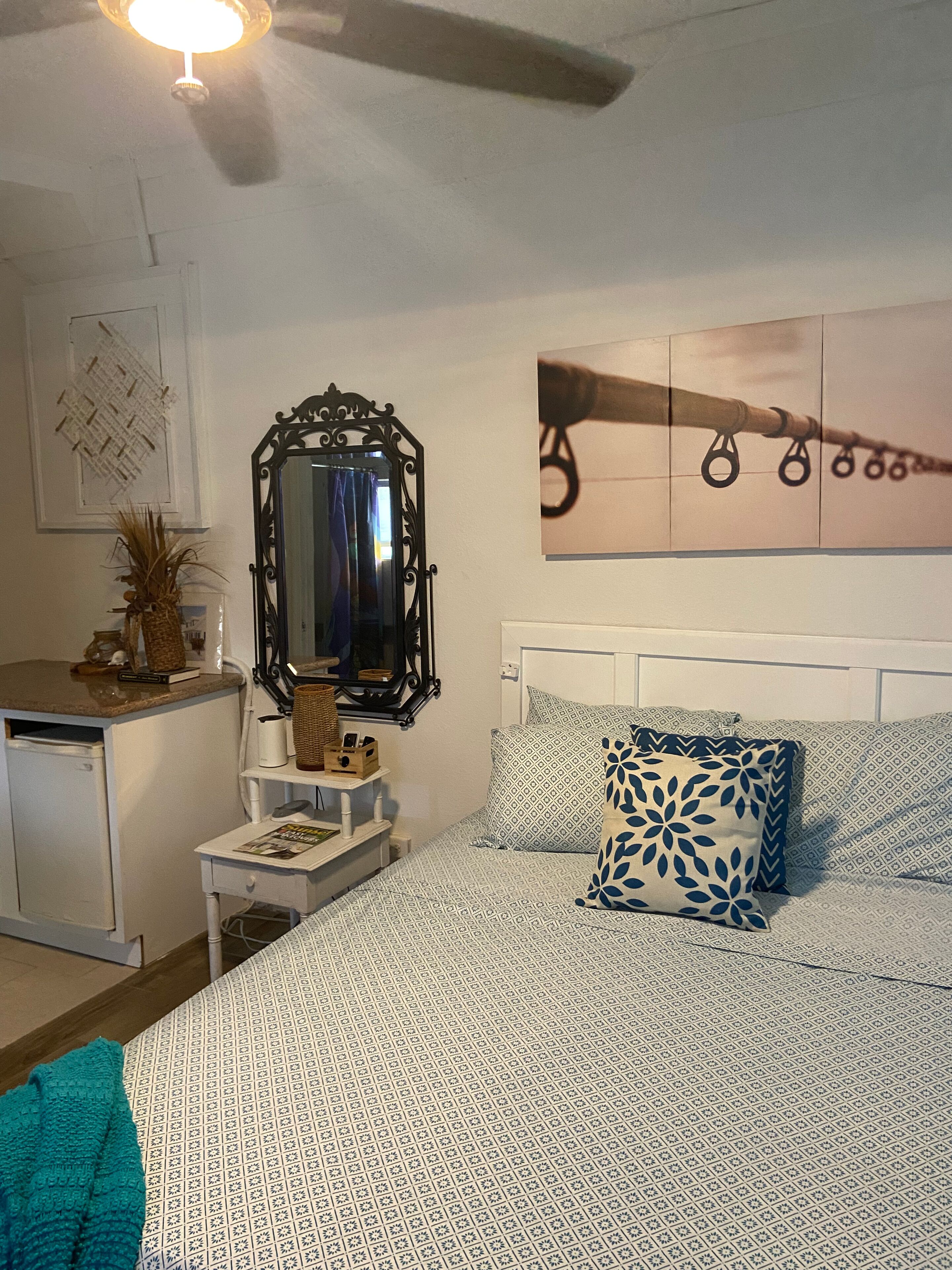 A bedroom with a bed, a dresser, a mirror, and a wall with a framed picture.