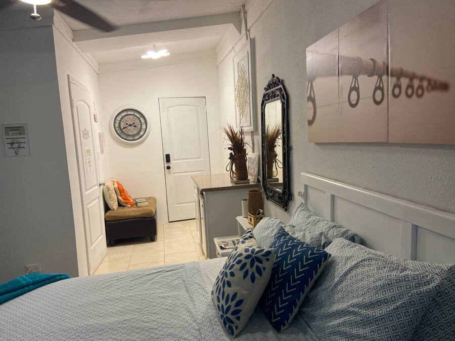 Een slaapkamer met een bed, nachtkastje, kapstok, spiegel en een deur naar een andere kamer.