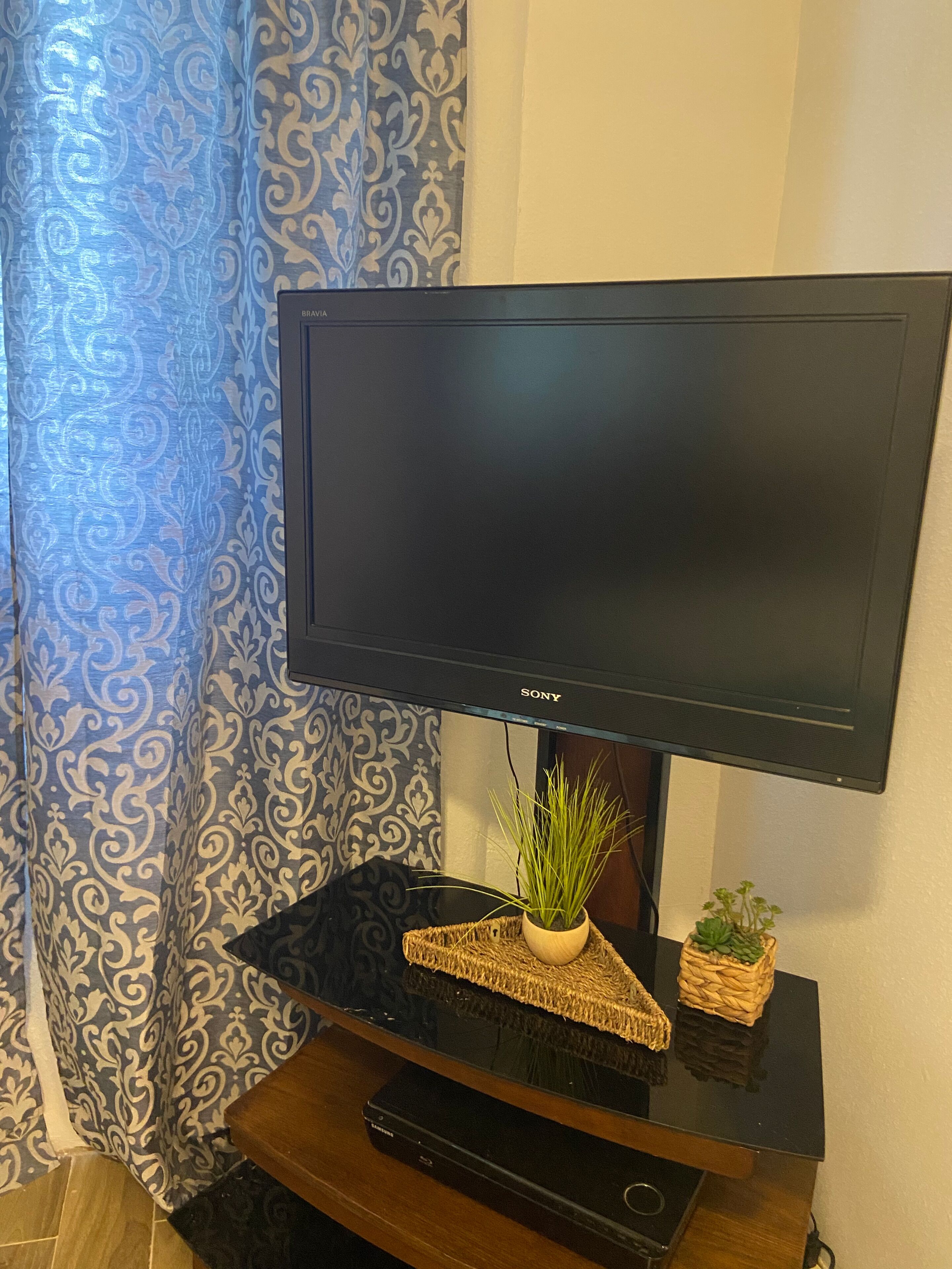 A flat-screen TV on a wooden stand with a plant and a small basket.
