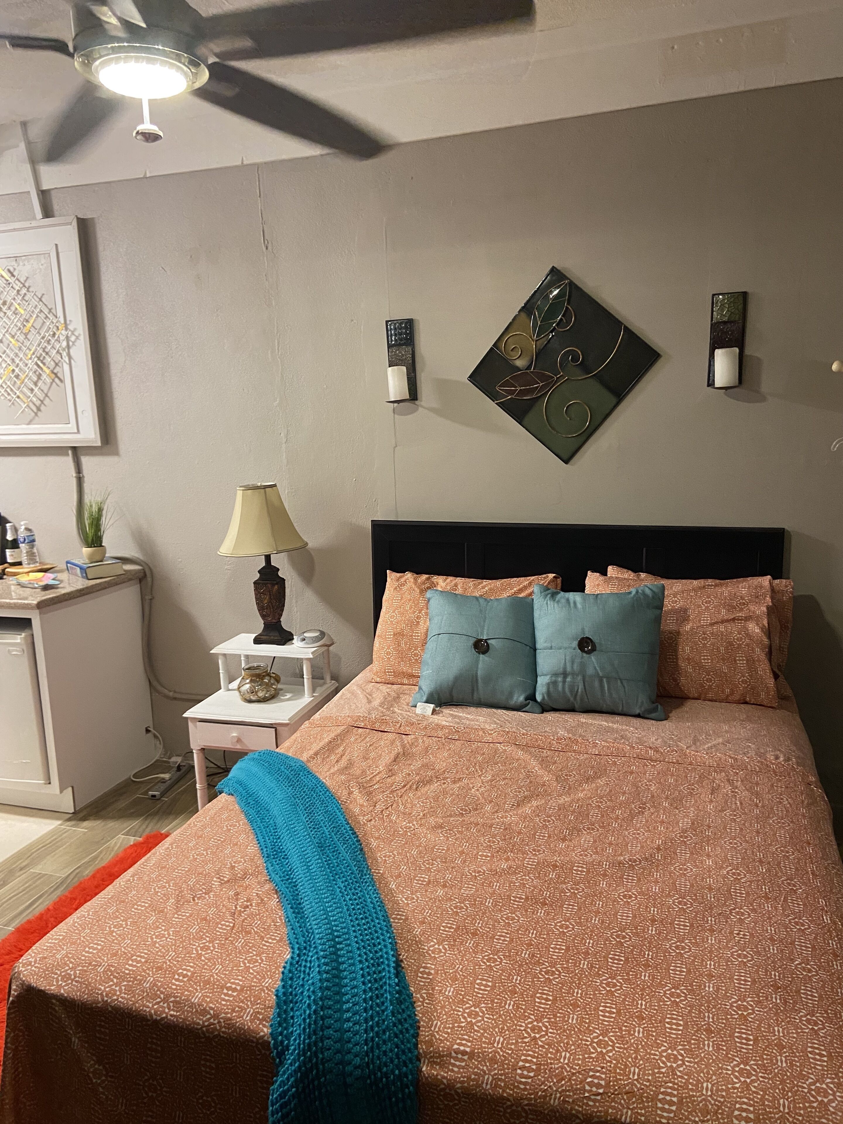A bedroom with a bed, a nightstand, a lamp, a ceiling fan, and wall art.