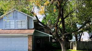 Une maison à deux étages avec un garage, une cheminée en briques et un grand arbre devant.