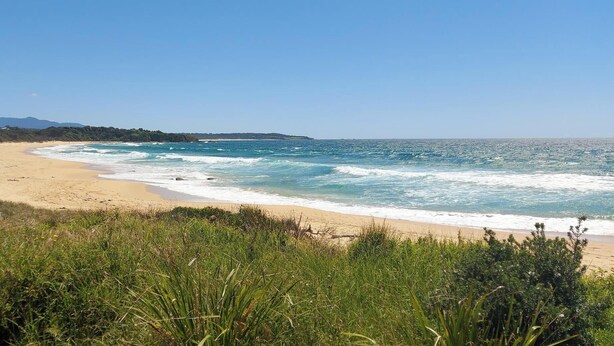 A beach with clear blue waters and a sandy shore, surrounded by greenery and a distant mountain. - Beach pad with a modern touch  in the heart of Iluka (Iluka)