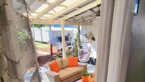 A covered outdoor seating area with a sofa and cushions, a hanging chair, and a potted plant. - Beach pad with a modern touch  in the heart of Iluka (Iluka)