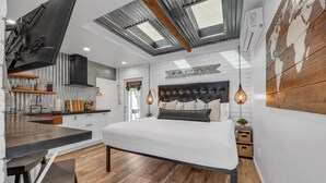 Quarto moderno com cama grande, claraboia, área de cozinha e piso de madeira.