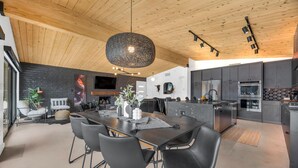 Uma cozinha moderna com armários escuros, uma ilha central e um lustre pendente.