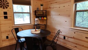 A wooden cabin interior with a round dining table, black chairs, a coffee machine, and a sign that reads "Travel the world, the way you want to." - The Redbud Cabin at Roman Nose (Watonga)