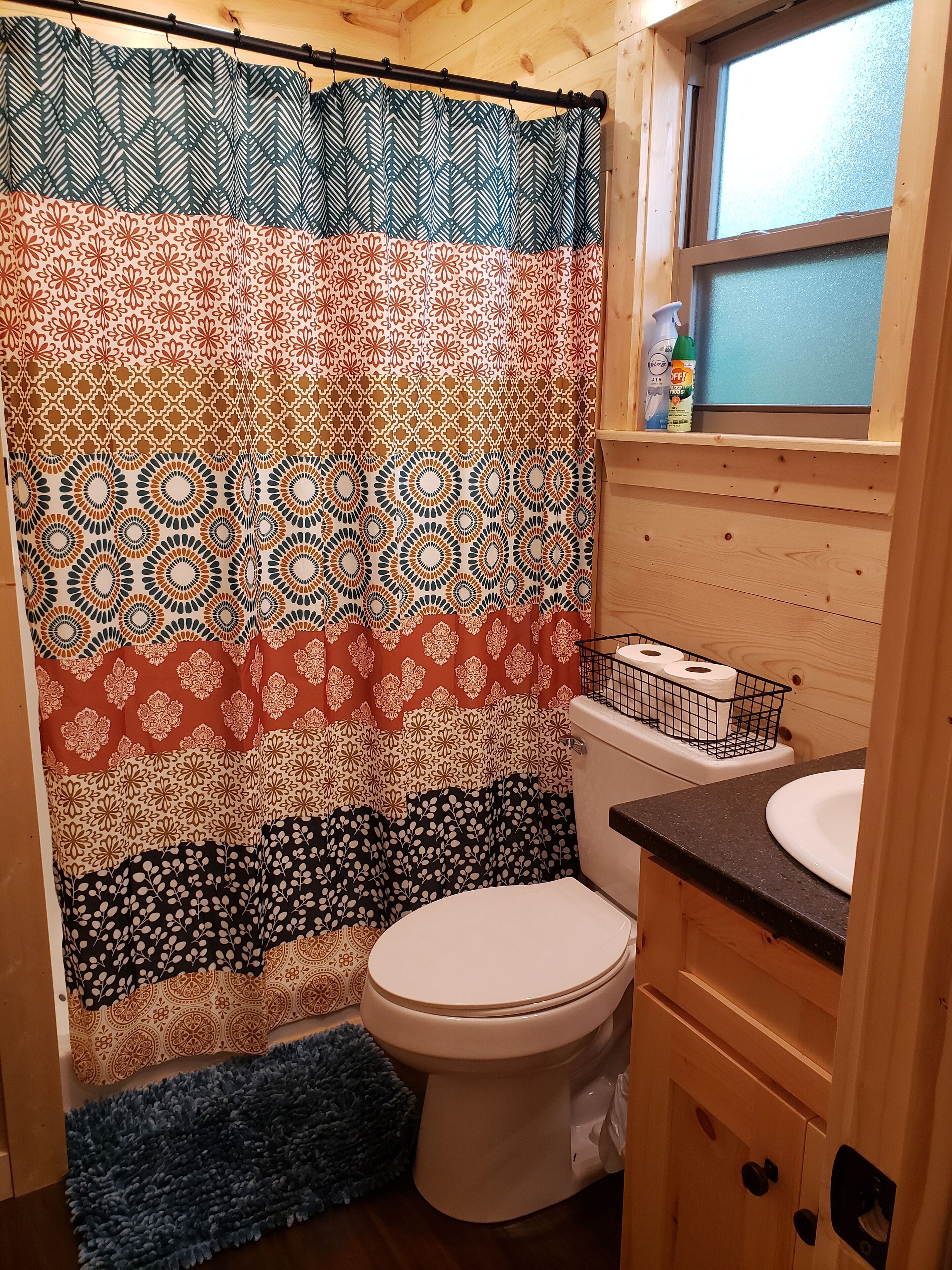 Ein Badezimmer mit einem gemusterten Duschvorhang, einer Toilette, einem Waschbecken und einem Fenster über dem Waschbecken.
