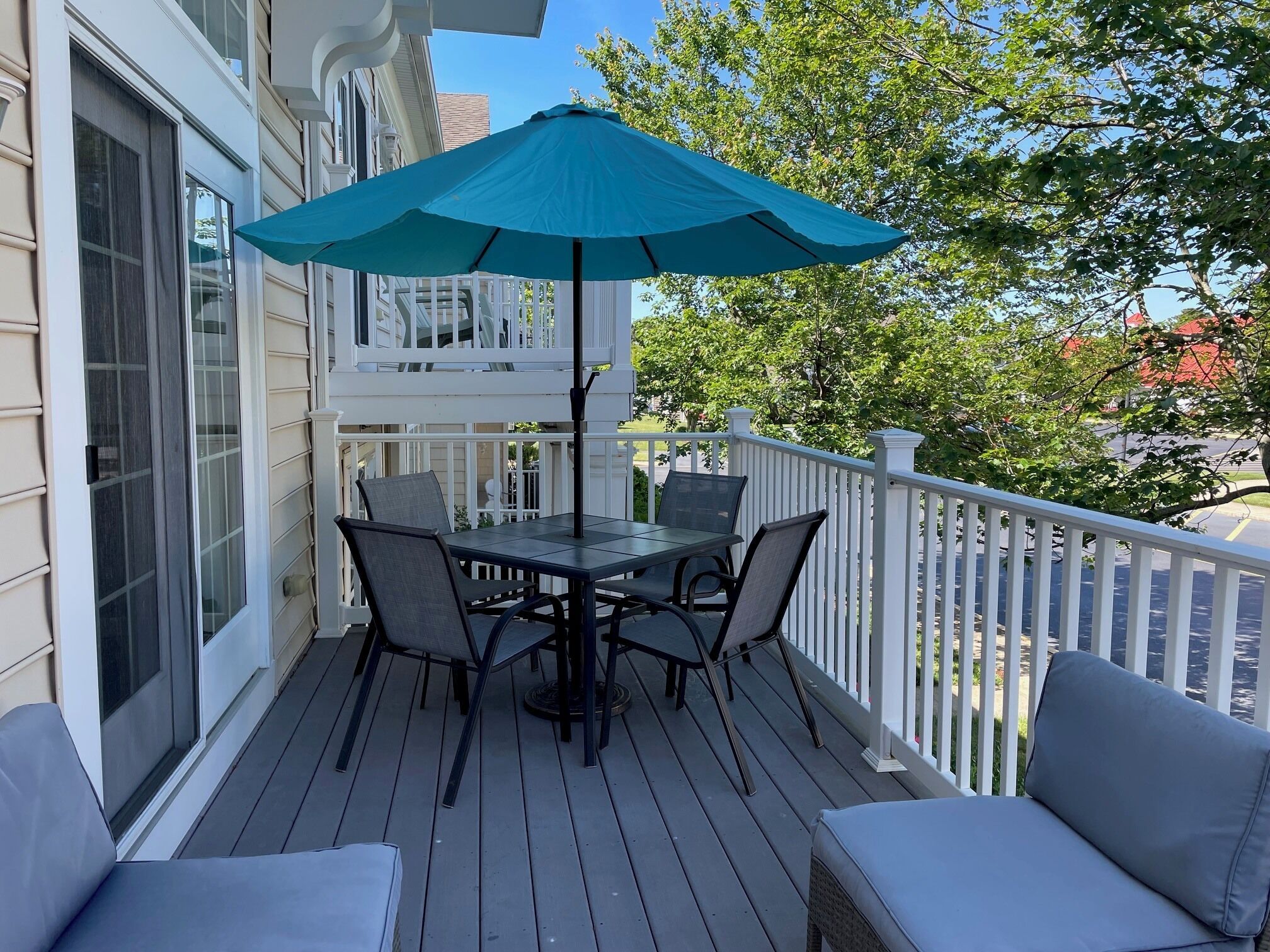 Een terras met een tafel en stoelen, een blauwe parasol en een witte reling.