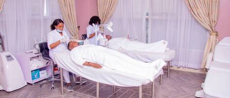 A medical facility with two patients lying on beds, a nurse attending to one patient, and another nurse preparing a treatment.