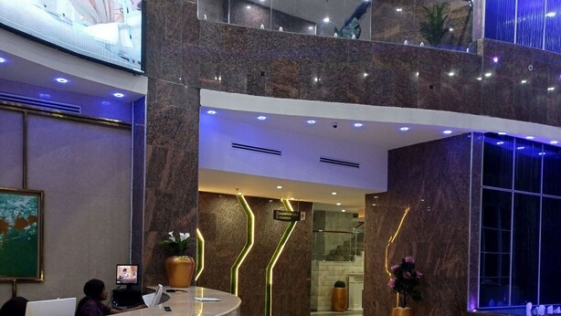 A modern hotel lobby with a reception desk, a large digital screen, and a staircase leading to an upper level. - Galaxy La Palm Royal Hotel (Port Harcourt)