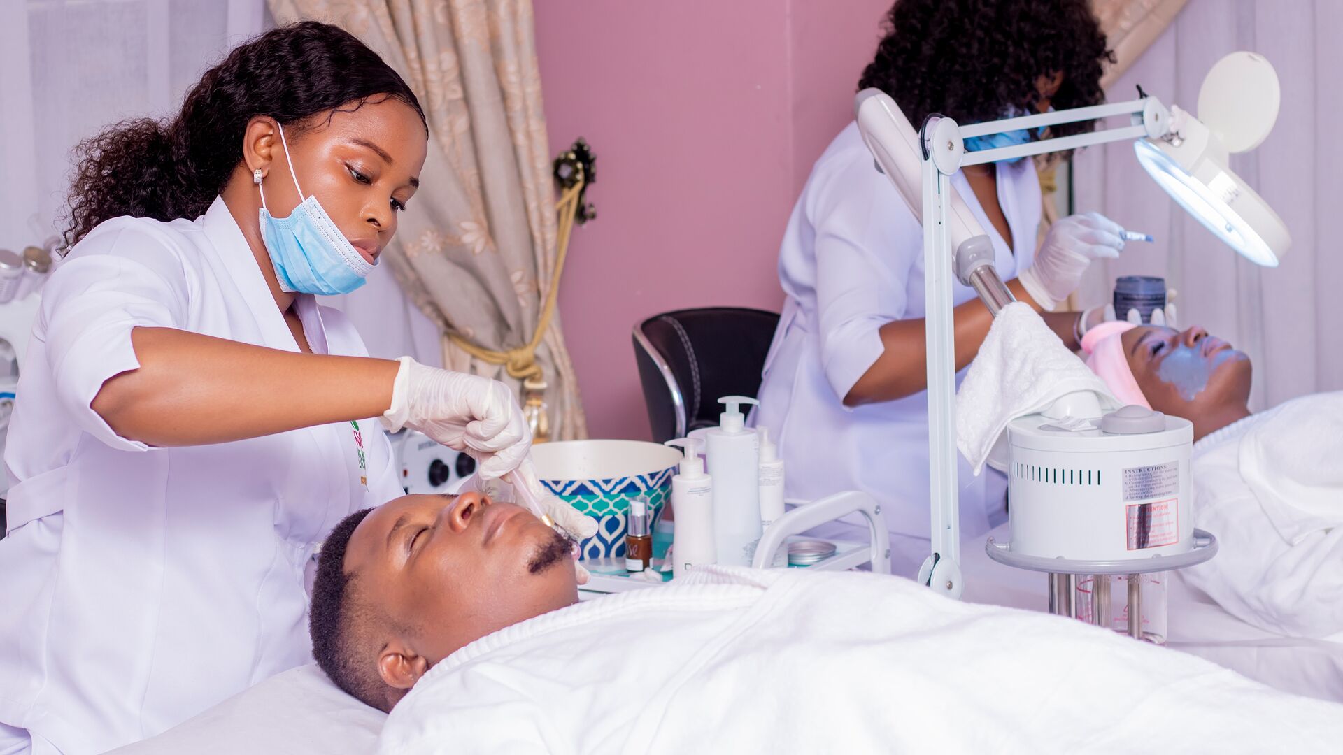 A medical procedure being performed in a clinical setting with a patient lying on a bed, a medical professional attending to the patient, and various medical equipment and supplies visible.