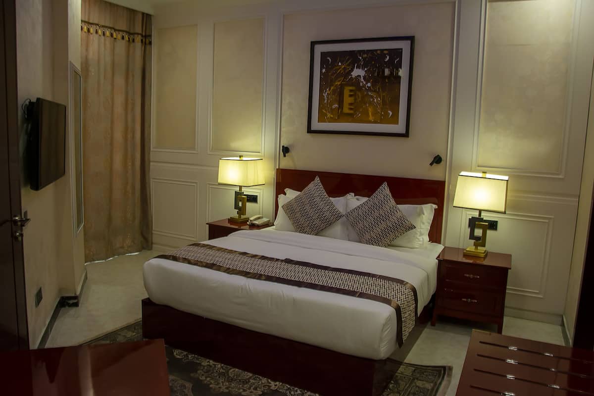 A hotel room with a large bed, two bedside tables with lamps, a framed picture on the wall, and a wooden nightstand.