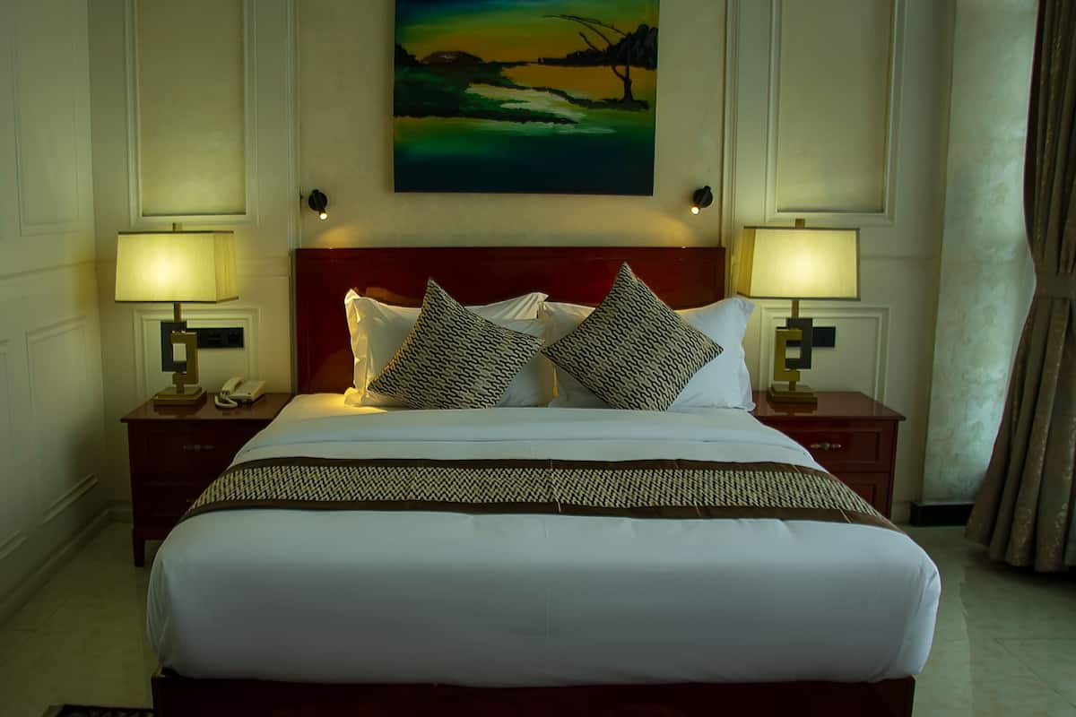 A hotel room with a large bed, two bedside lamps, a nightstand with a phone, and a painting above the bed.
