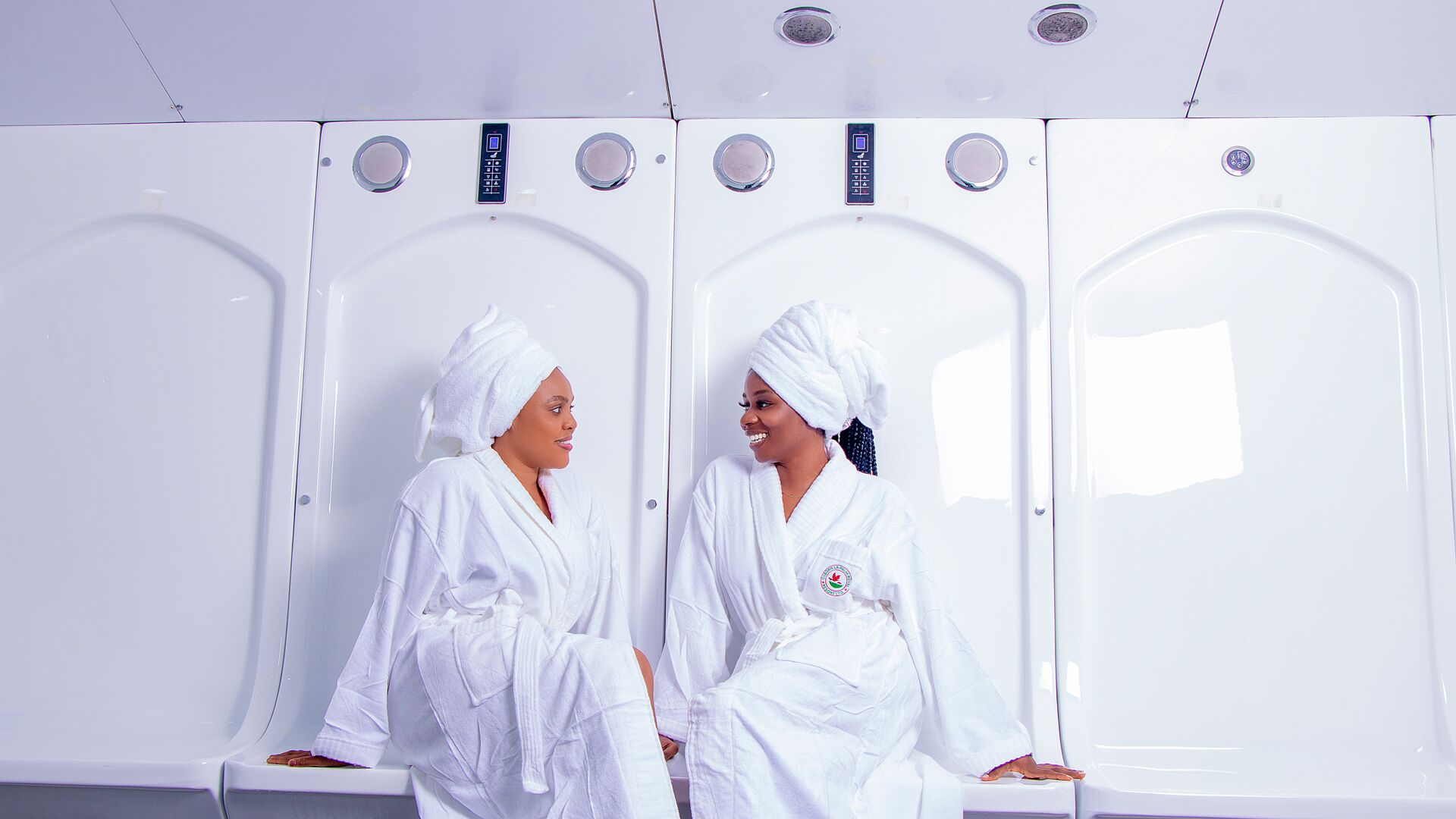 A row of white sauna cabins with control panels and a logo on the wall.
