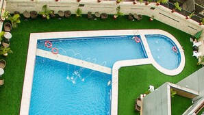 A rectangular swimming pool with a smaller circular section, surrounded by a white deck and green artificial grass. - Galaxy La Palm Royal Hotel (Port Harcourt)