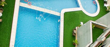 A rectangular swimming pool with a smaller circular section, surrounded by a white deck and green artificial grass.