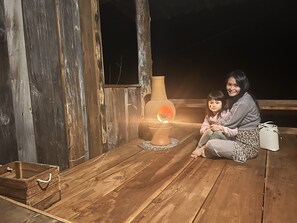 Una terraza de madera con un hogar rústico, un pequeño cofre y un banco.