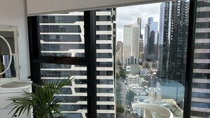 A modern bedroom with a large window offering a city view, a bed, a chair, and a potted plant. - 3 bedroom apartment in the heart of the CBD. (Melbourne)