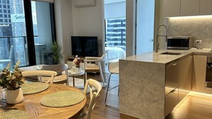 A modern kitchen with a marble countertop, a built-in microwave, and a sink. There is a dining area with a wooden table and white chairs. - 3 bedroom apartment in the heart of the CBD. (Melbourne)
