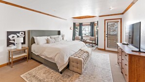 A bedroom with a large bed, a wooden nightstand, a TV, and a window with blinds. - Luxe Chalet - Sleeps 15 (Midway)