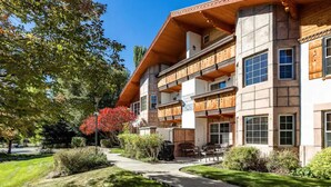 A multi-story building with a wooden balcony, a covered outdoor seating area, and a well-maintained garden. - Luxe Chalet - Sleeps 15 (Midway)