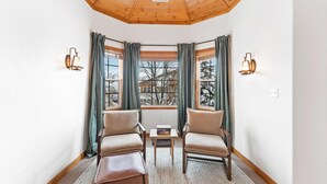 A cozy corner room with two leather chairs, a small table, and a view of a snowy landscape through large windows with curtains. - Luxe Chalet - Sleeps 15 (Midway)
