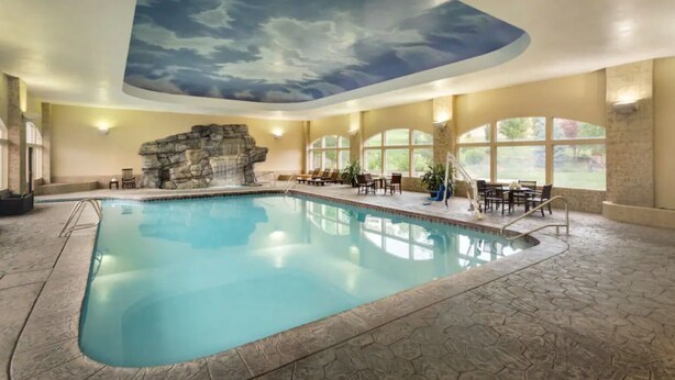 An indoor swimming pool with a stone wall and a rock formation, surrounded by lounge chairs and tables. - Luxe Chalet - Sleeps 15 (Midway)